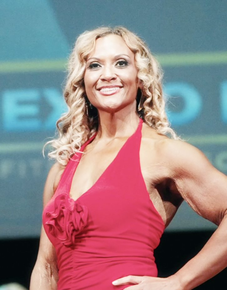 Person with curly blonde hair smiles while wearing a red dress.